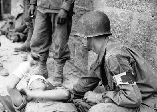 An Aidman of the Medical Detachment, 16th Infantry Regiment treats a wounded German prisoner during fighting in Sicily. 