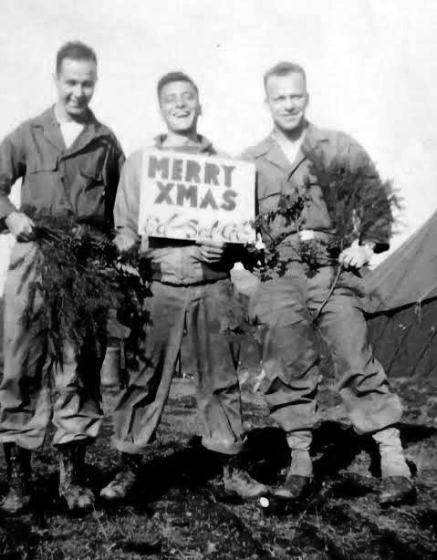 Three members of the 107th Evacuation Hospital fooling around with a sign wishing everyone a “Merry Christmas”. Probably taken while the organization was billeted at the Collège Turenne, Sedan, France, from 22 December 1944 until 21 January 1945.