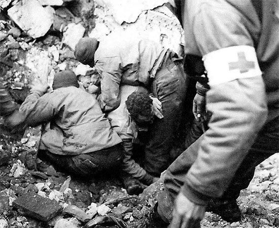 Vintage photo illustrating a GI buried in debris following an enemy bombing, being freed by medical personnel. Photo taken in Italy in January 1944.