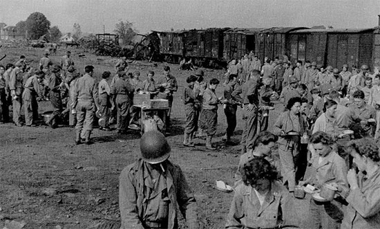 Picture of 58th General Hospital personnel enjoying some food, during a stop while traveling to La-Haye-du-Puits, Normandy. A partially destroyed train is visible in the background.