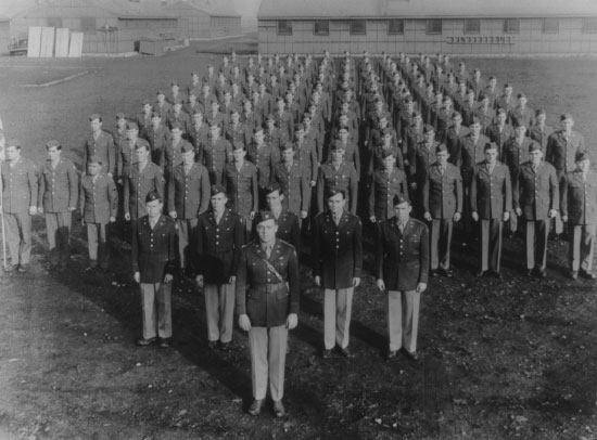 Photograph showing personnel of the 603d Quartermaster Graves Registration Company at Fort Lewis, Washington, 23 December 1943. The Service Club is in the left background, while barracks buildings are behind the men. 